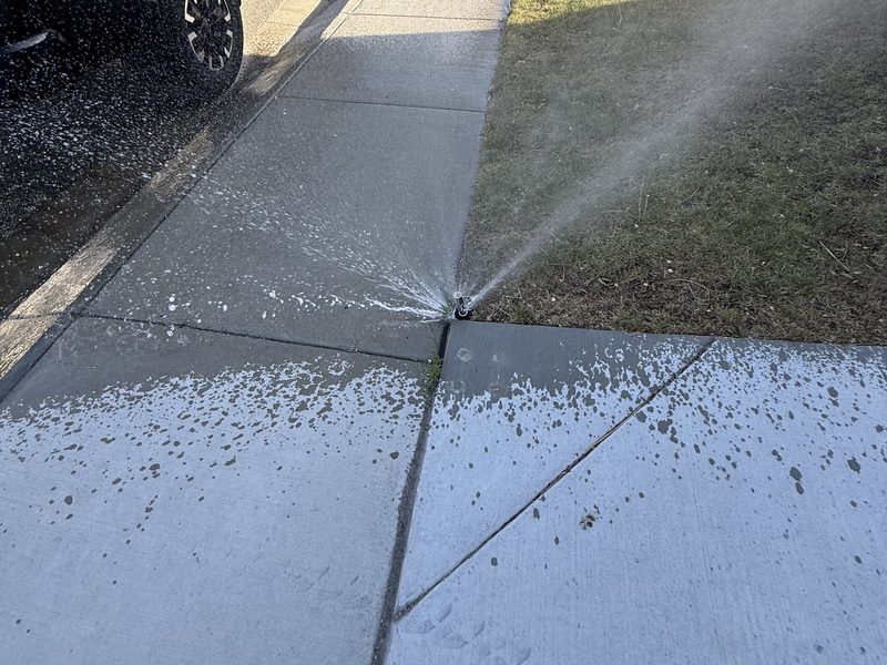 Broken sprinkler head spraying water onto a sidewalk instead of the lawn in Sparks, Nevada